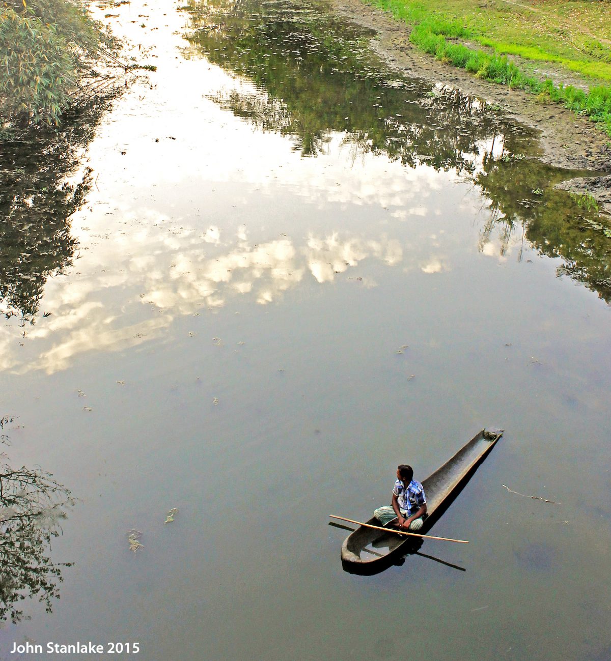 A Man And His Boat: The waterways of Bangladesh provide crucial trading and transport links throughout the country, and they are filled each day with boats of varying shapes and sizes. Here in Jessore district, John encountered this boatman enjoying a quiet moment on the water in the late afternoon.