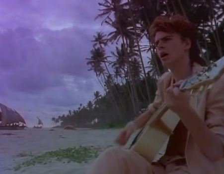 Bassist John Taylor strumming on acoustic by the beach. Credit: YouTube.